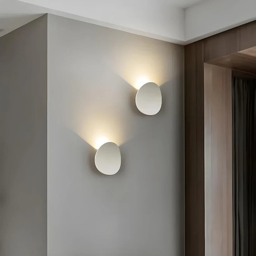 Luminária de parede escultural em metal com iluminação suave e difusa, ideal para ambientes contemporâneos e sofisticados.