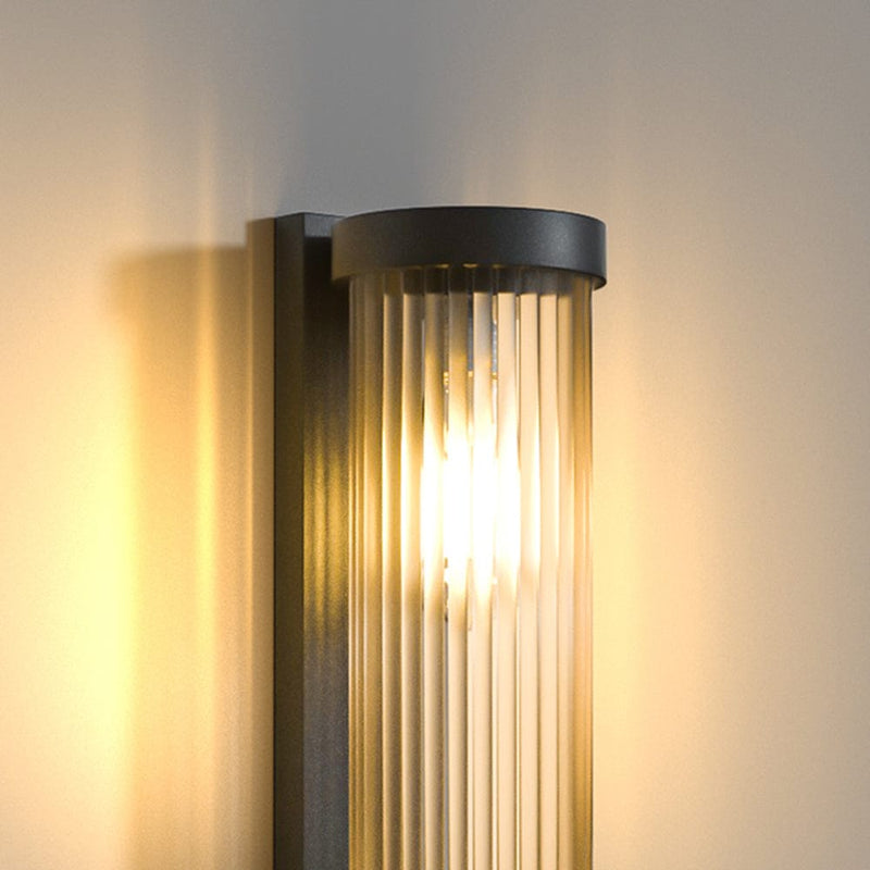 Luminária externa cilíndrica de metal e vidro, resistente à água IP65 com design moderno.
