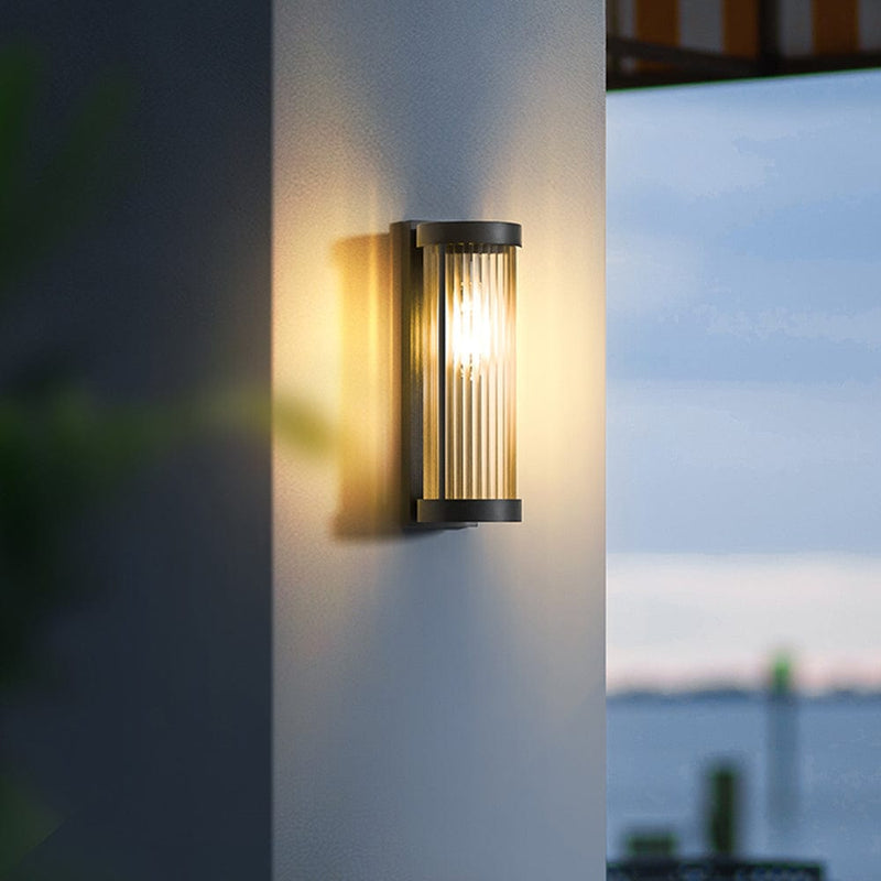 Luminária externa cilíndrica de metal e vidro, resistente à água IP65 com design moderno.